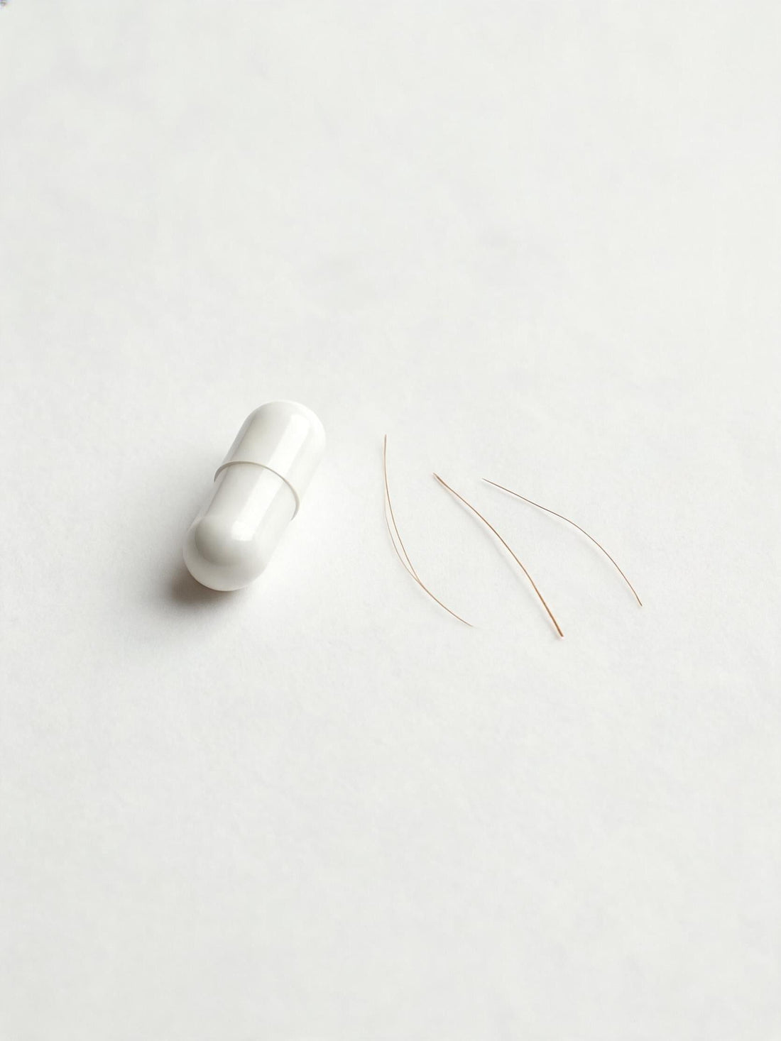 A single zinc mineral capsule beside a few loose hair strands on a plain surface, representing the question of whether zinc affects hair and scalp health.